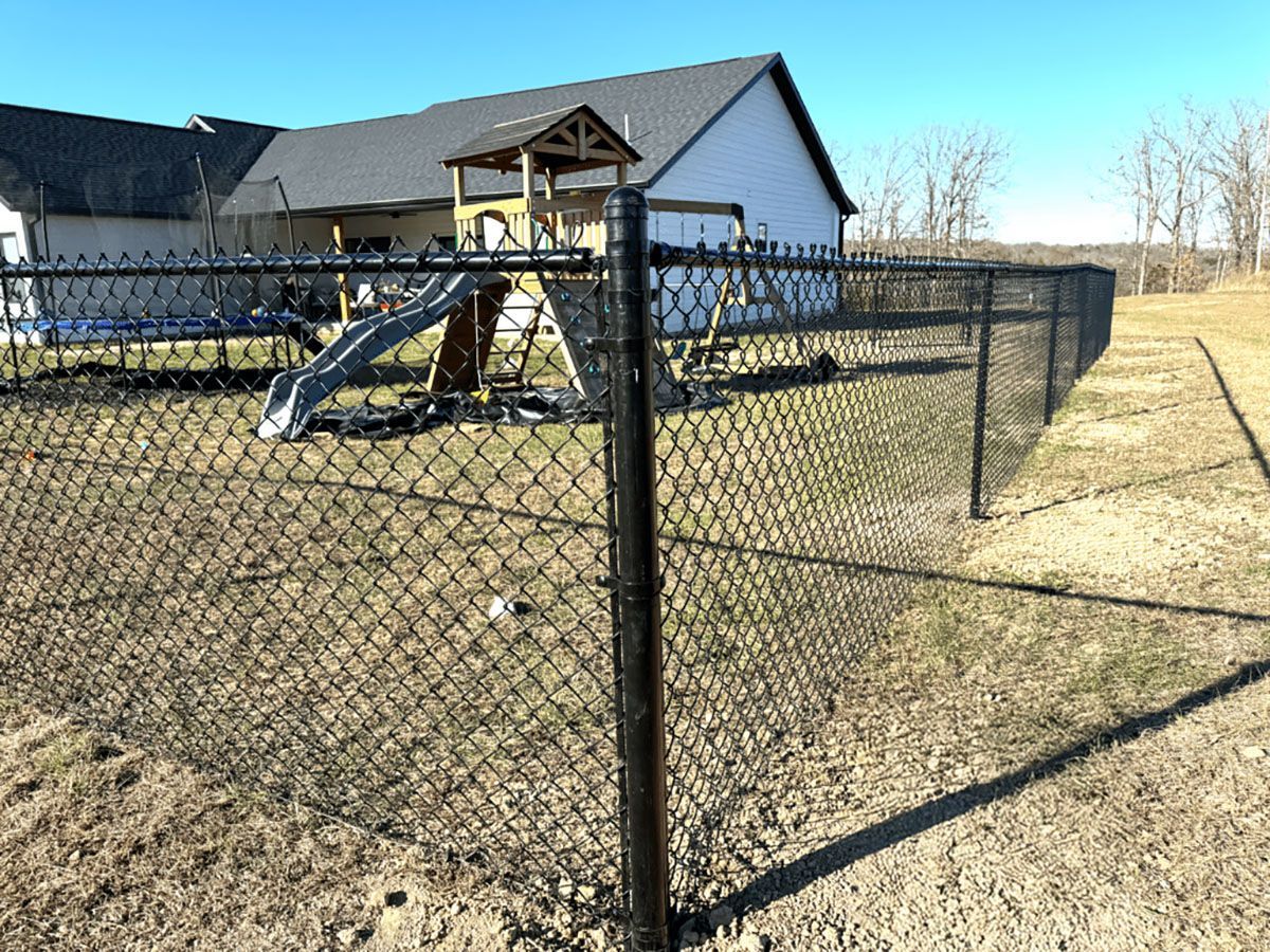 A chain link fence surrounds a playground in front of a house.
