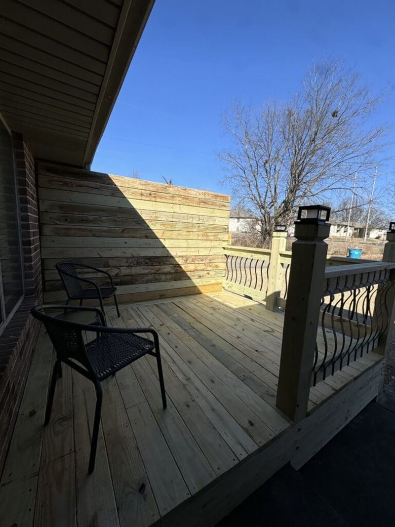 A wooden deck with chairs and a railing on a sunny day.