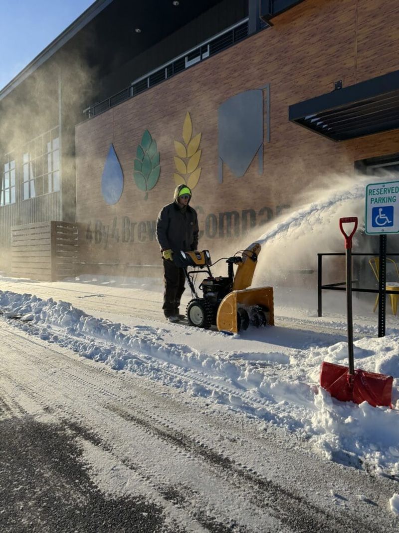 A man is blowing snow from a snow blower on the side of the road.
