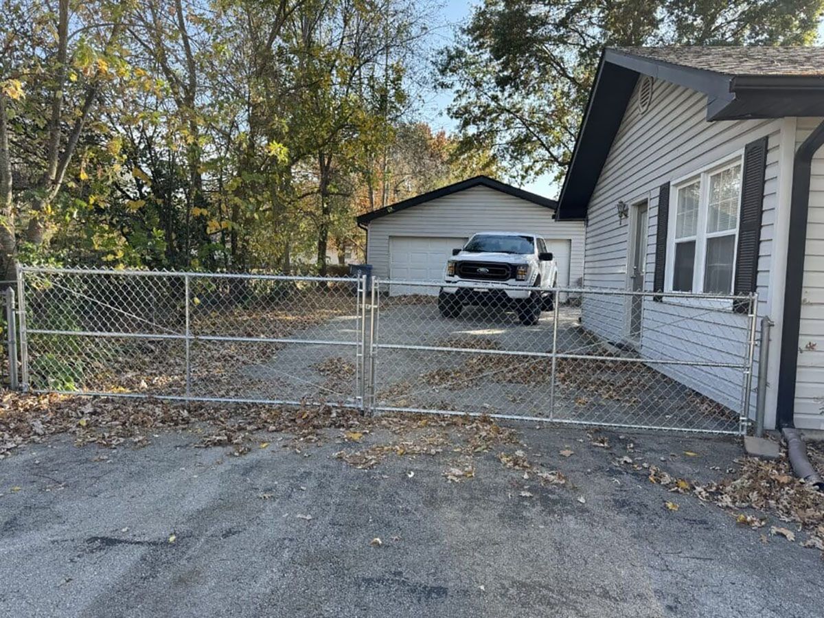 A white truck is parked in front of a white house behind a chain link fence.