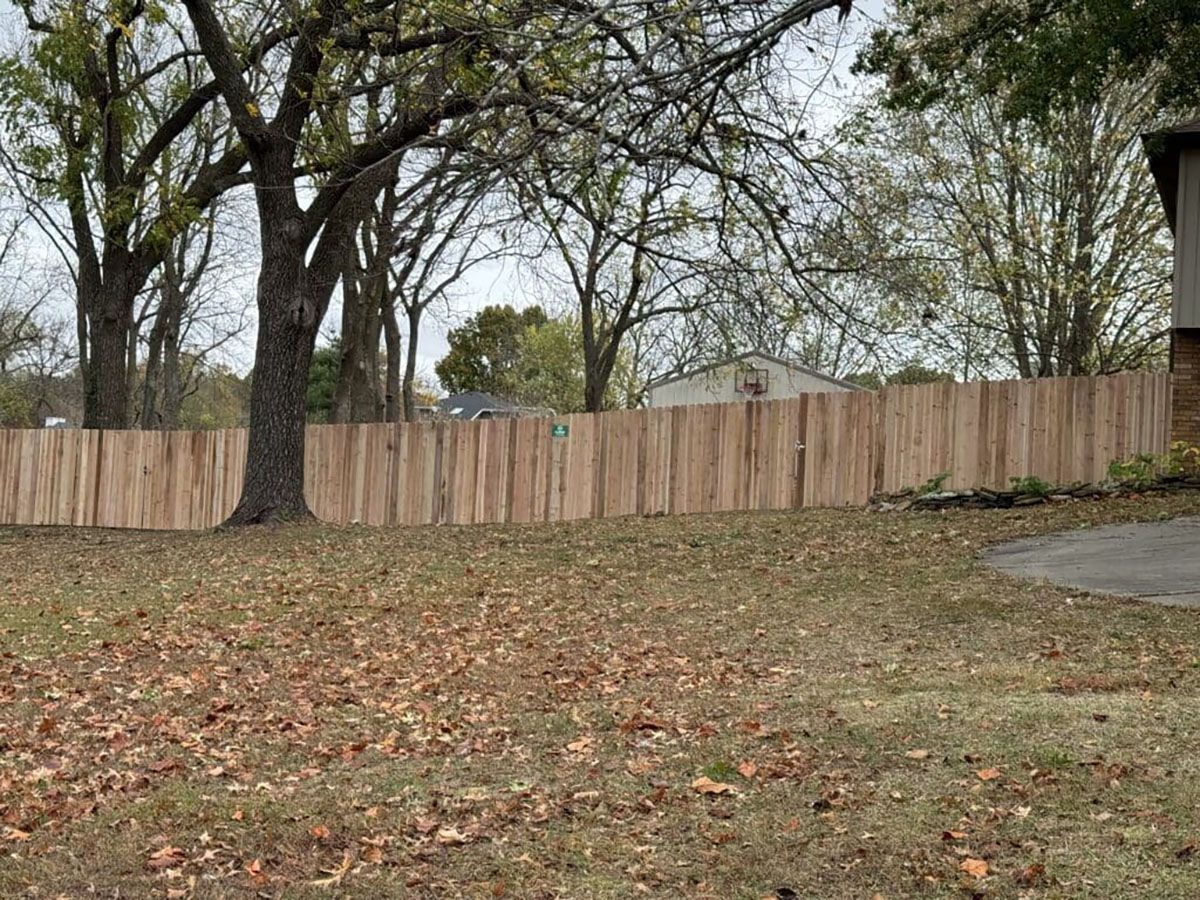A wooden fence surrounds a lush green field with trees in the background.
