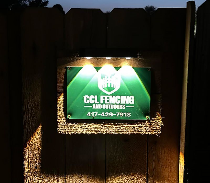 A sign on a wooden fence that says ccl fencing and outdoors is lit up at night.