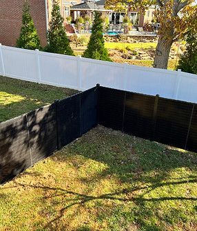 A white fence is surrounded by a black fence in a backyard.