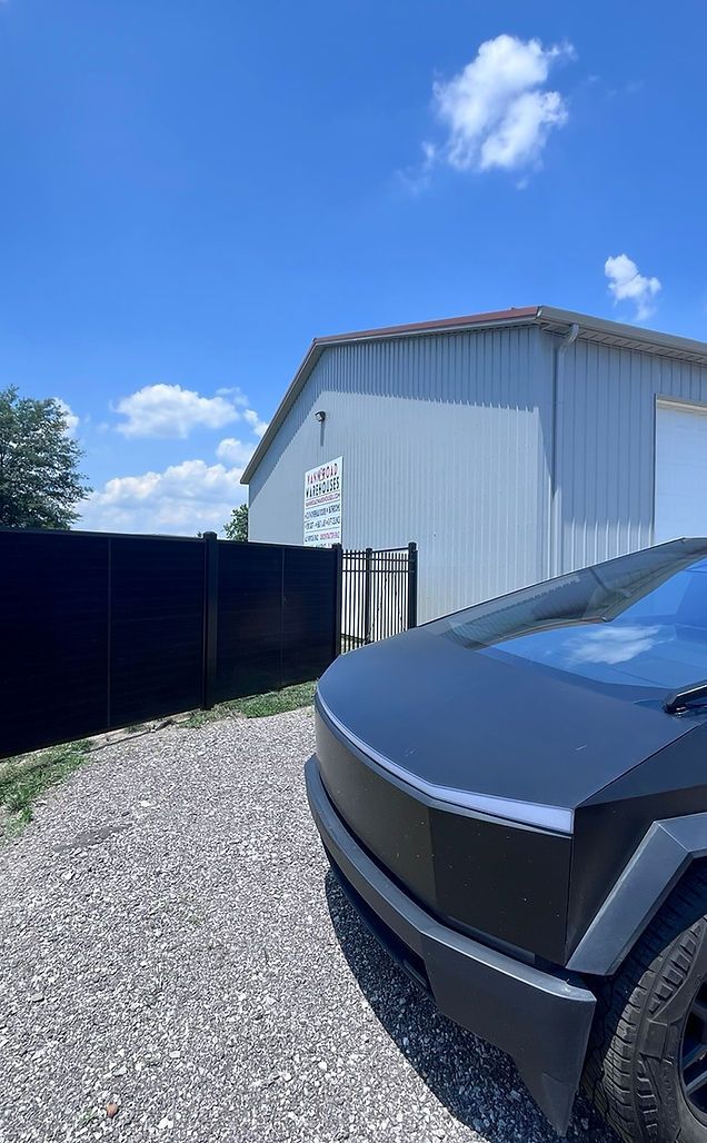 A black car is parked in a gravel driveway in front of a garage.