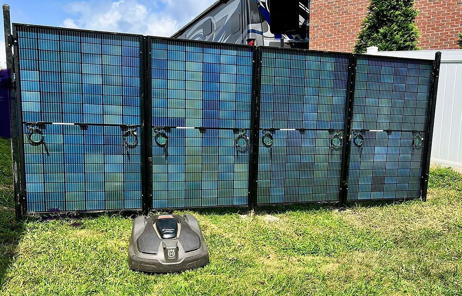 A lawn mower is sitting in front of a fence made of solar panels.
