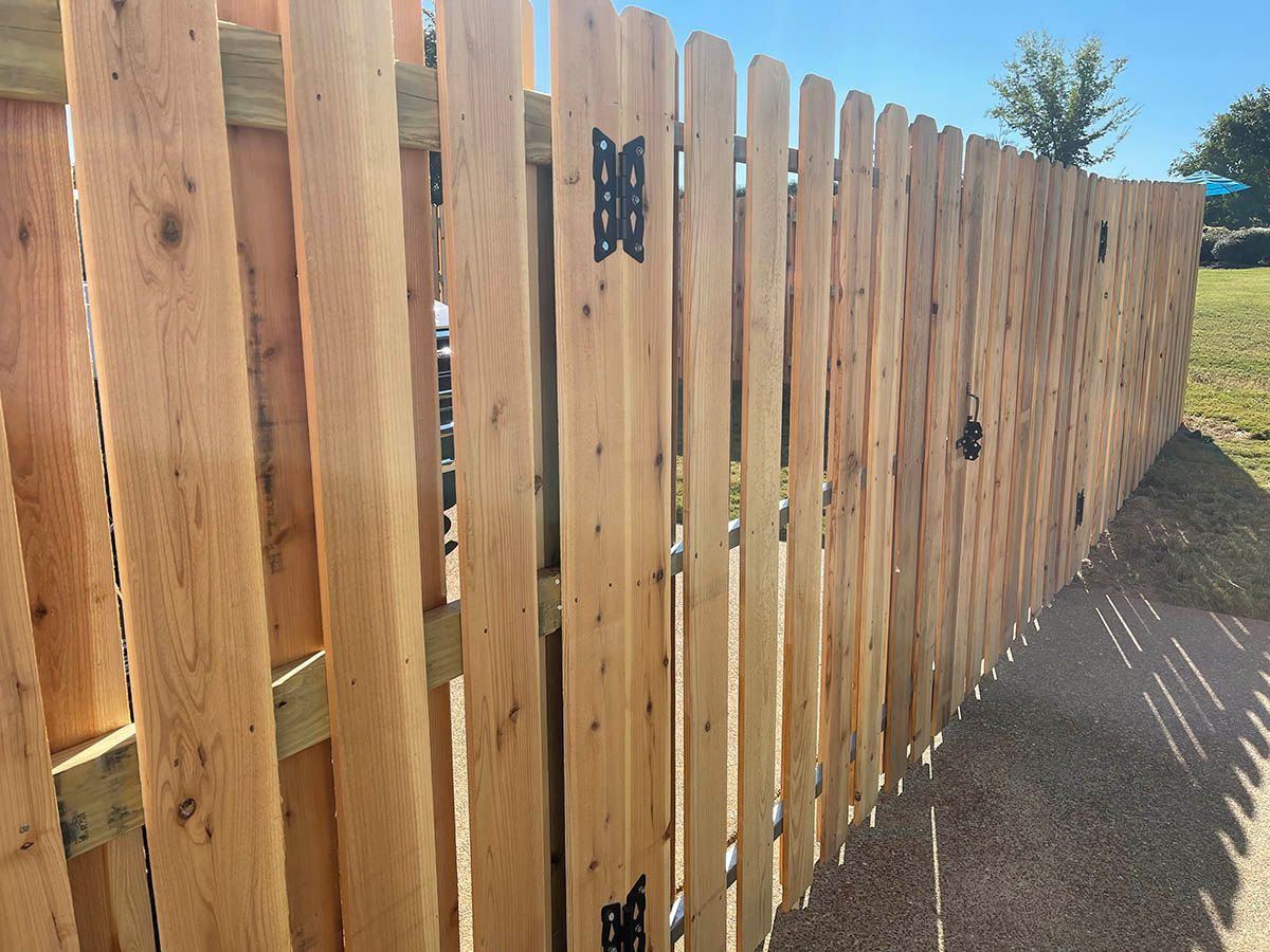 Wooden fence with vertical planks, metal hinges, and gate, outdoors on a sunny day.