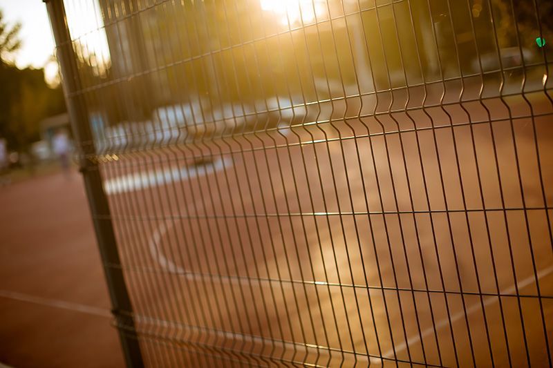A fence surrounding a basketball court with the sun shining through it.