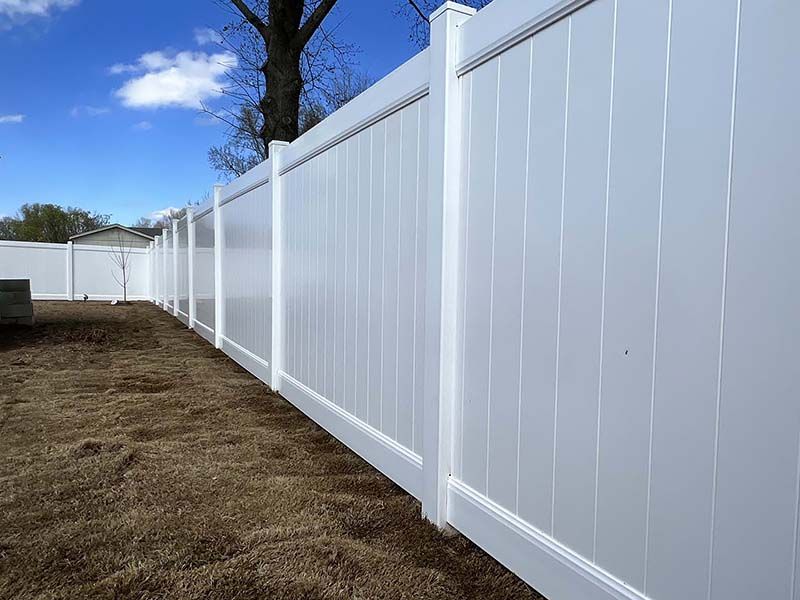 A white vinyl fence surrounds a dirt yard with a tree in the background.