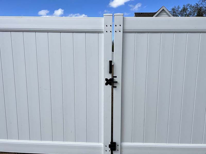 A white fence with a black gate and a blue sky in the background.