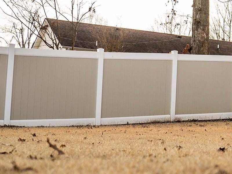 A white and tan fence is in the backyard of a house.