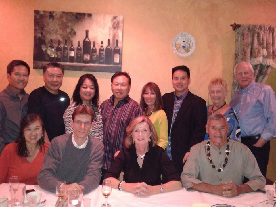 Group of people, likely a celebratory gathering, seated around a table, and smiling at the camera.