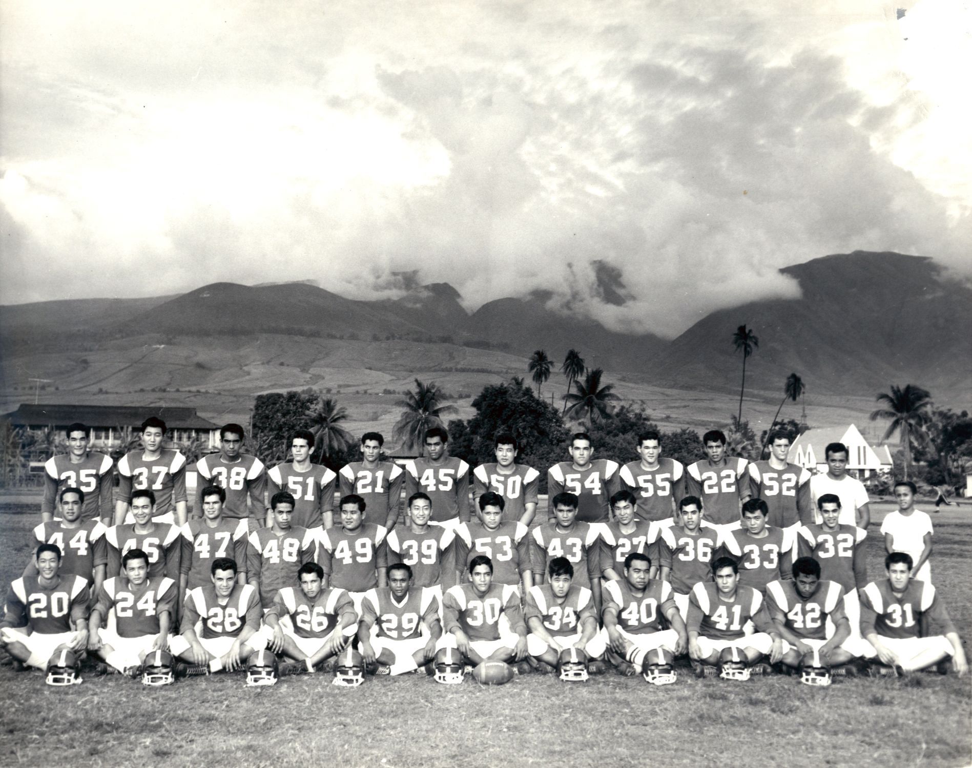 A vintage black and white photo of a football team posing on a field with mountains in the background. 