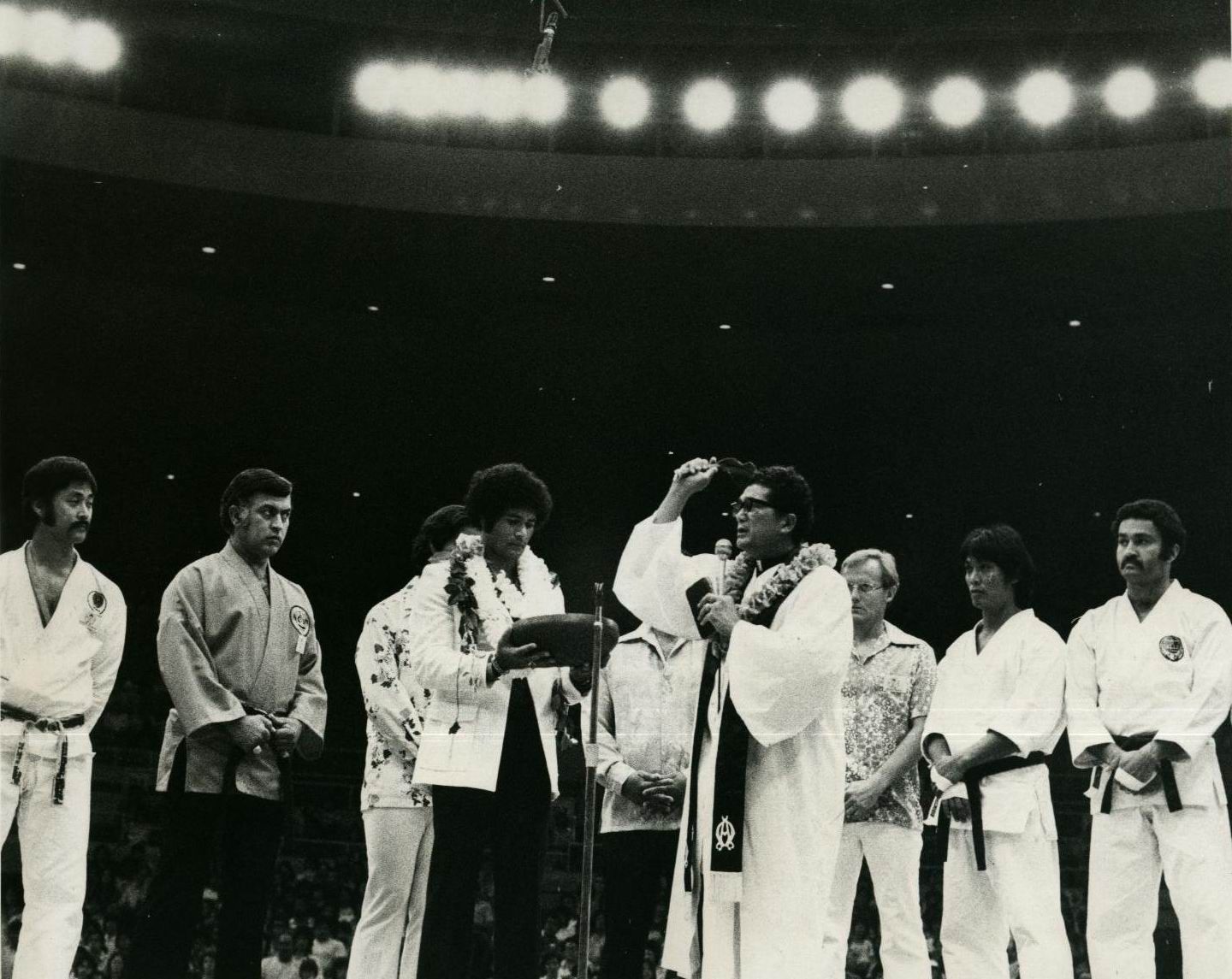 Group of people on a stage, one wearing a lei and receiving an award. Others wear martial arts uniforms.