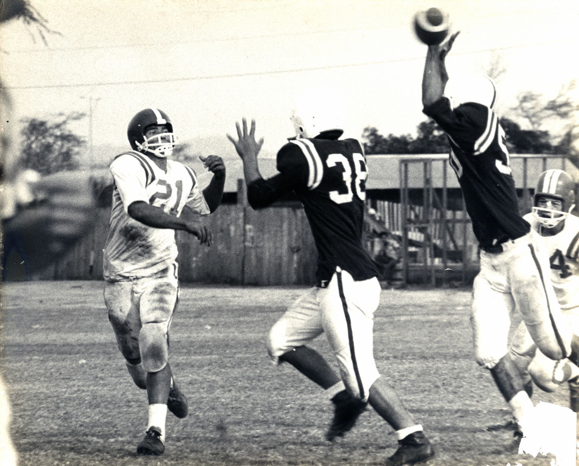 Football players in action. A player in a dark jersey attempts to catch a high pass.