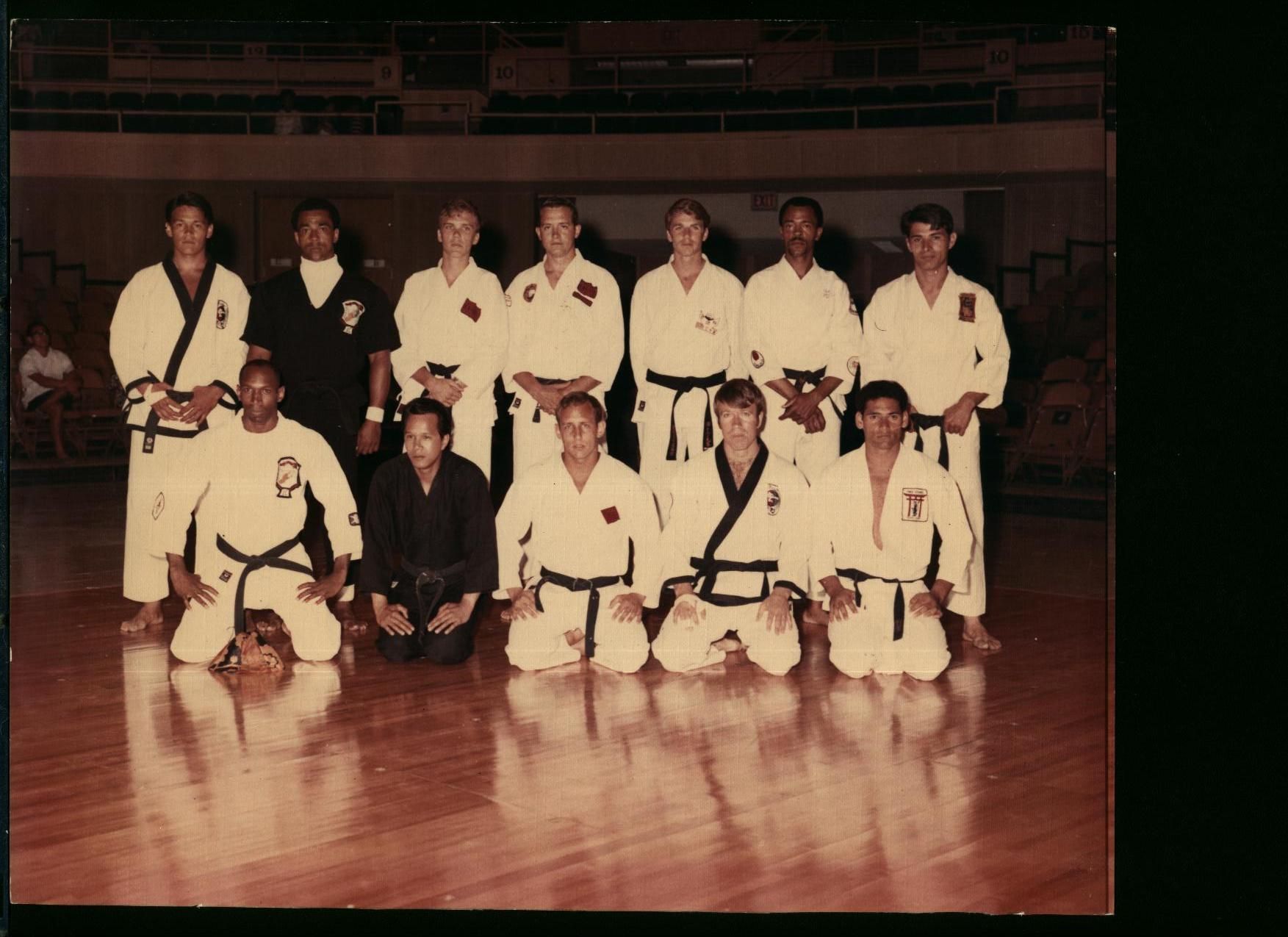 A group of people in karate uniforms pose on a wooden floor.