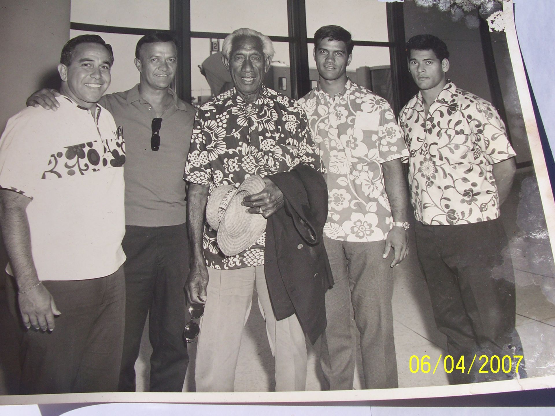Group photo: Five men pose together. An elderly man in a floral shirt is flanked by younger men in casual shirts. 