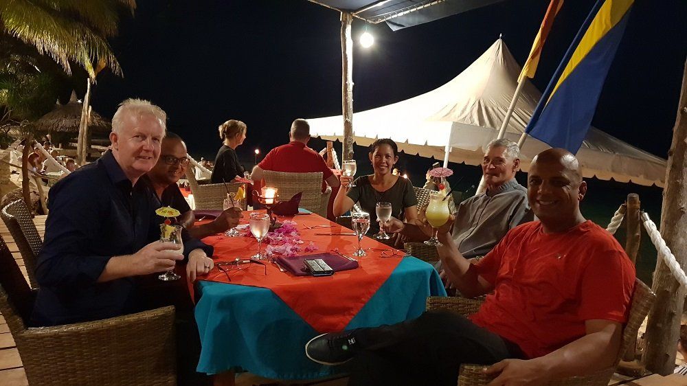 Group of people at an outdoor restaurant, toasting with drinks at a table decorated for a celebration, at night.