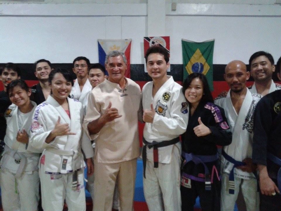 Group of people in martial arts attire posing for a photo indoors, some flashing thumbs up.