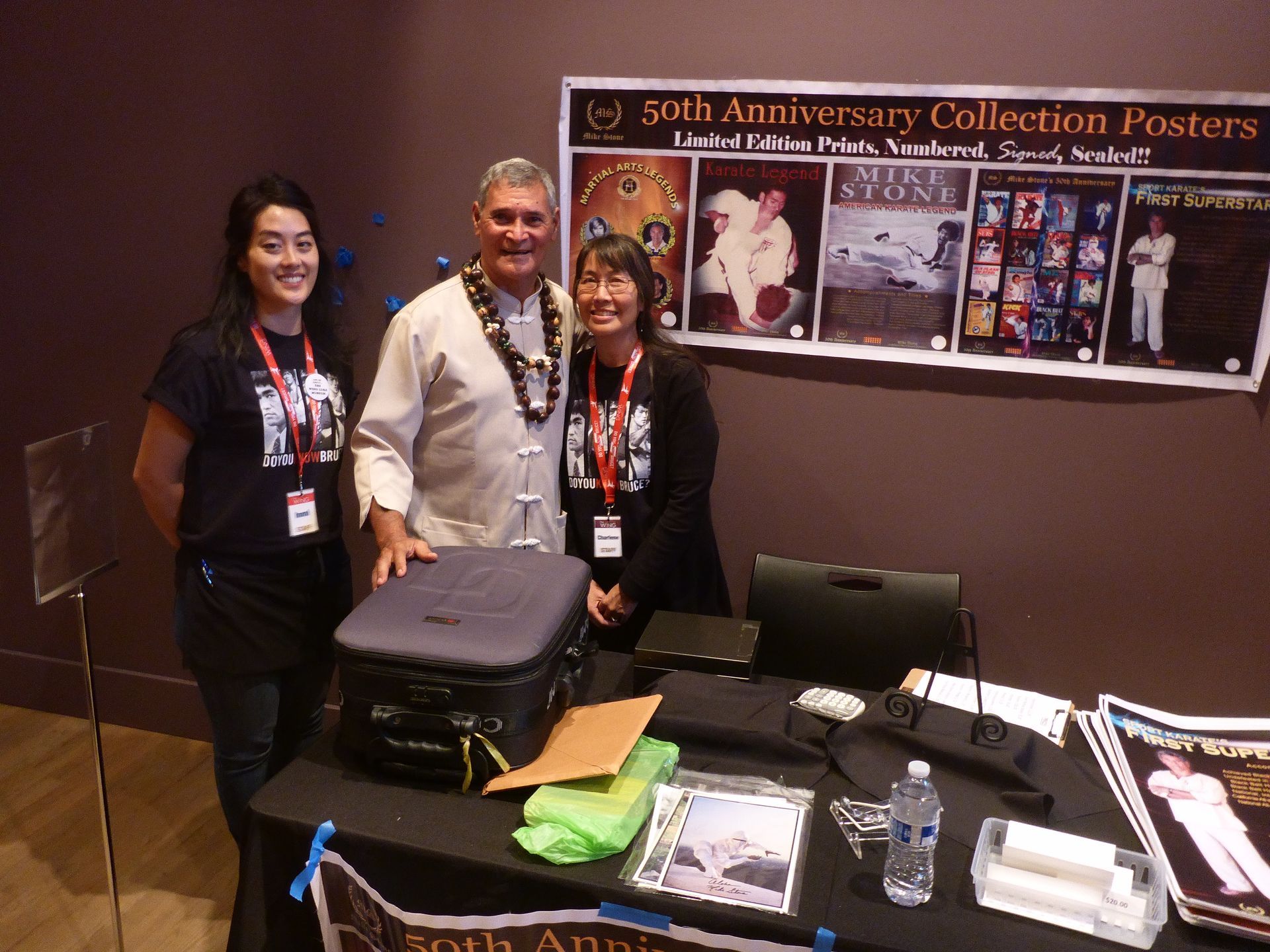 Three people stand at a booth with posters and merchandise. 