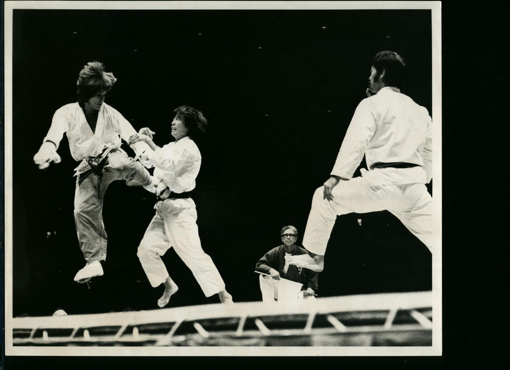 Judo match in progress: Two athletes in white uniforms are airborne mid-kick and pose.