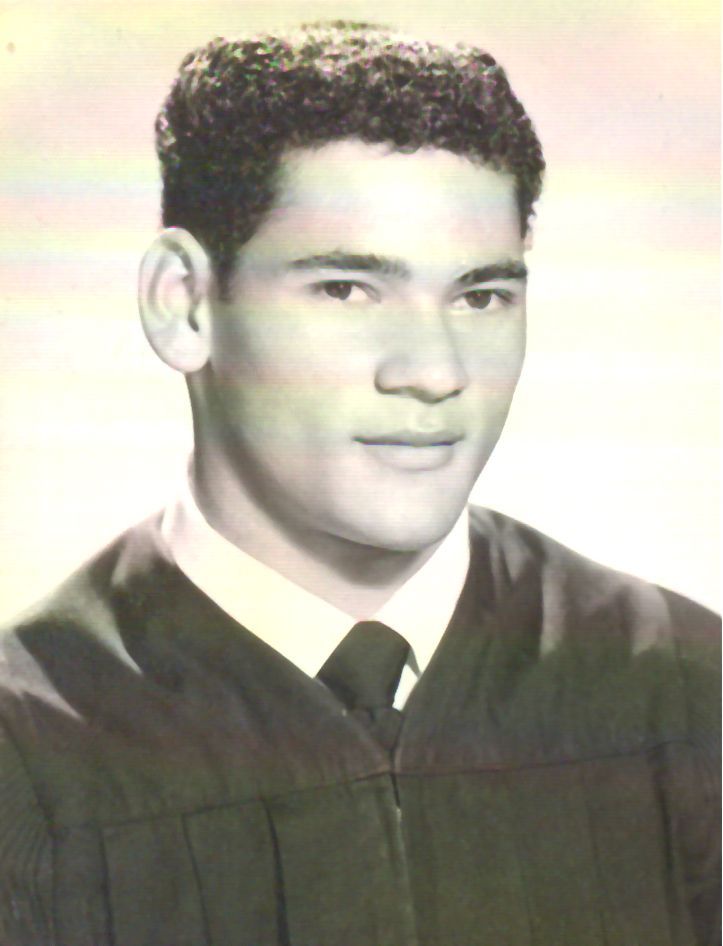 Young man in a graduation gown, looking at the viewer. He has short, dark hair, tan skin, and a serious expression.