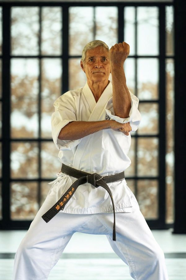 Karate instructor in white gi with black belt, demonstrating technique to group of students.