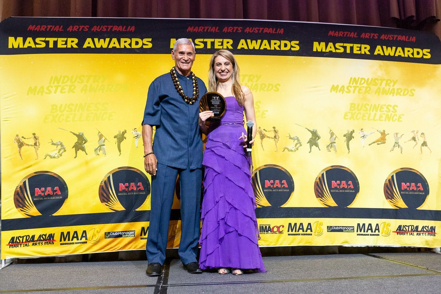 A man and woman pose with an award at a martial arts event.