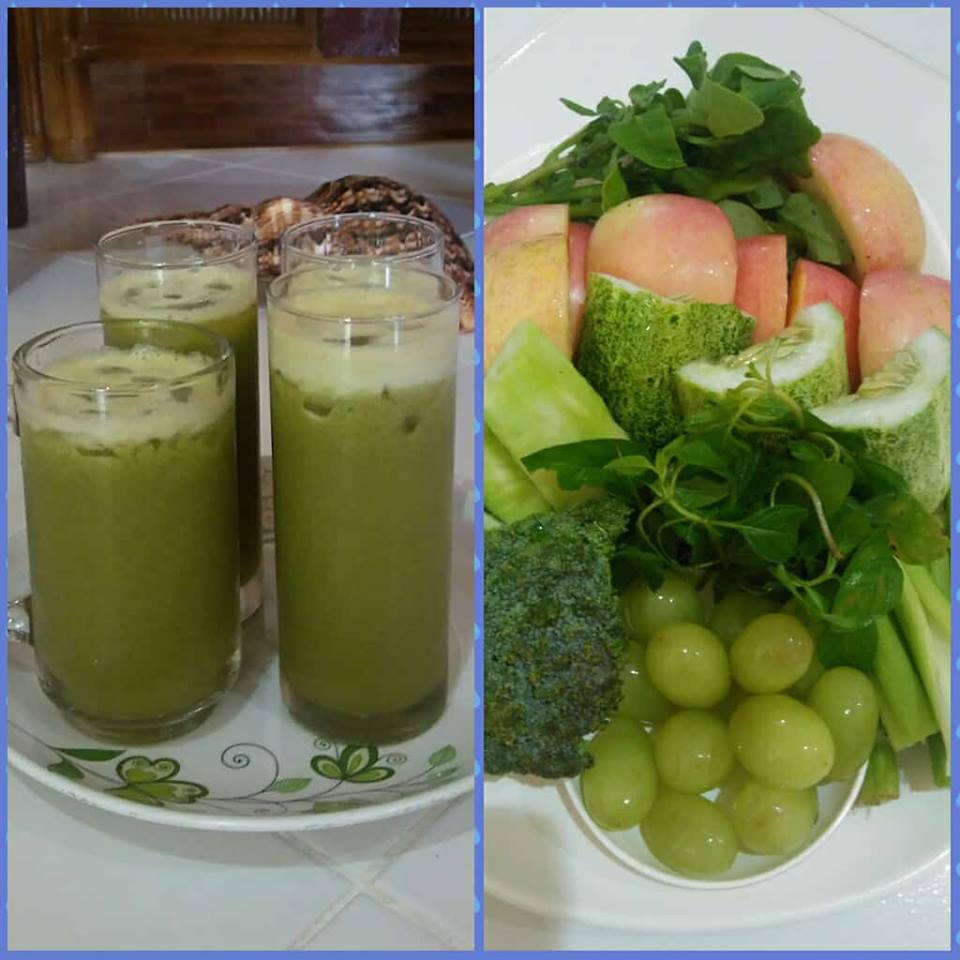 Green juice in glasses, and a plate of fresh fruit and vegetables, including apples, grapes, cucumbers, and broccoli.