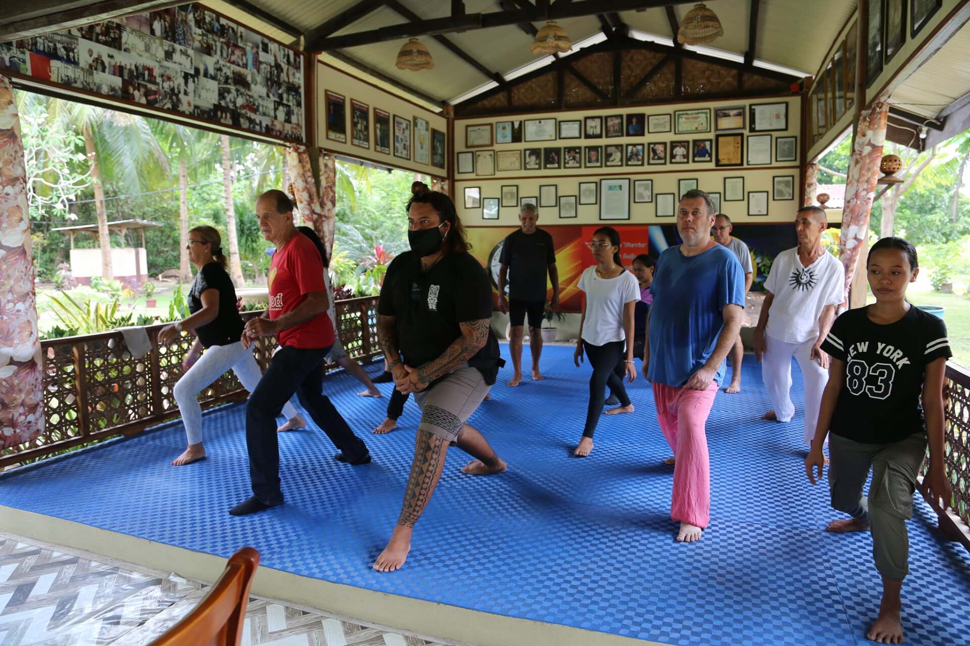People doing exercises on a blue mat in an outdoor building. There are photos on the walls.