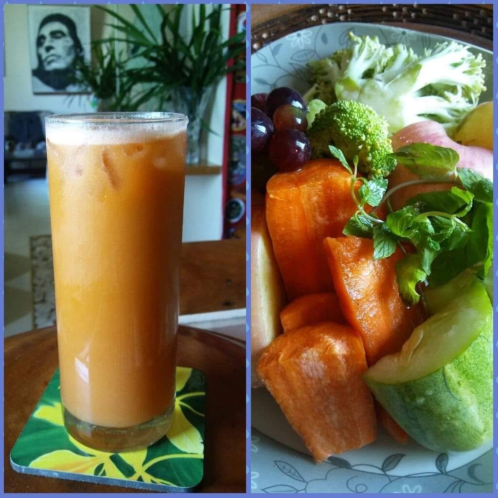 A tall glass of orange juice with ice next to a plate of carrots, grapes, and broccoli.
