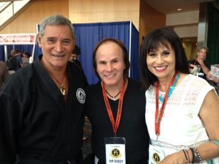 Three people posing together; an older man in a black martial arts uniform, a man in a black shirt.