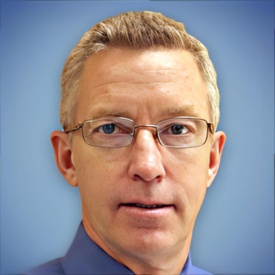 A man wearing glasses and a blue shirt looks at the camera