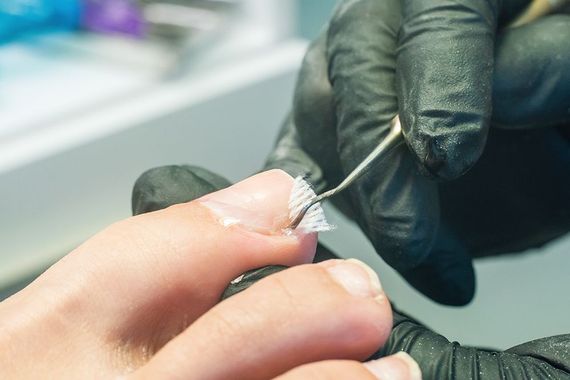 A person is getting their toenails done by a nail artist wearing black gloves.