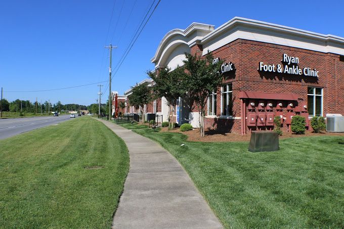 A sidewalk leading to a brick building with a sign that says ryan foot & ankle clinic.