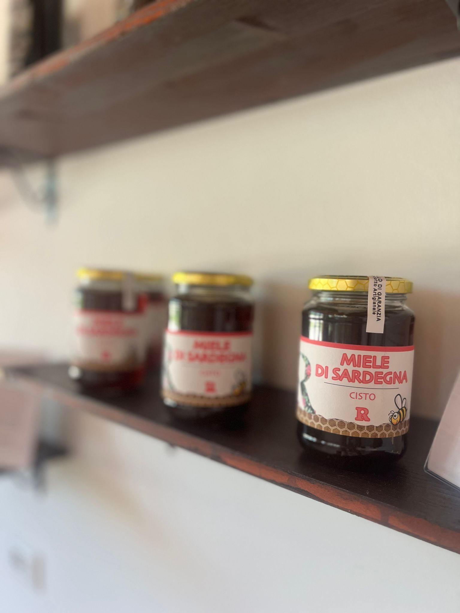 Tre barattoli di miele sono appoggiati su uno scaffale di legno.