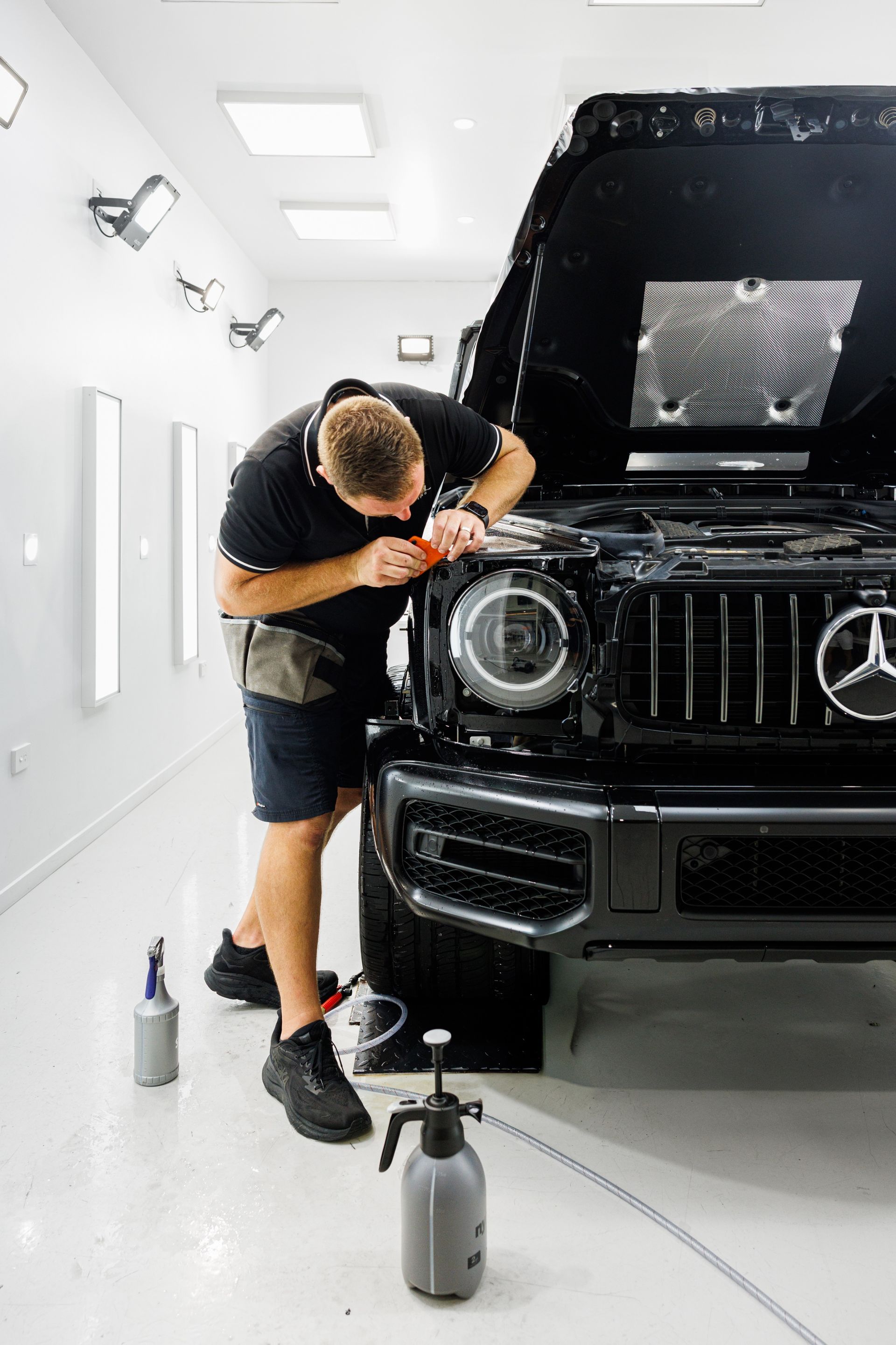 Clear protective film applied to the rear bumper of a gray car in a shop.