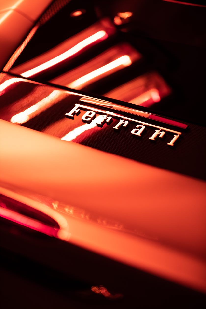 Shiny red Ferrari logo on a car with reflections of red lights.
