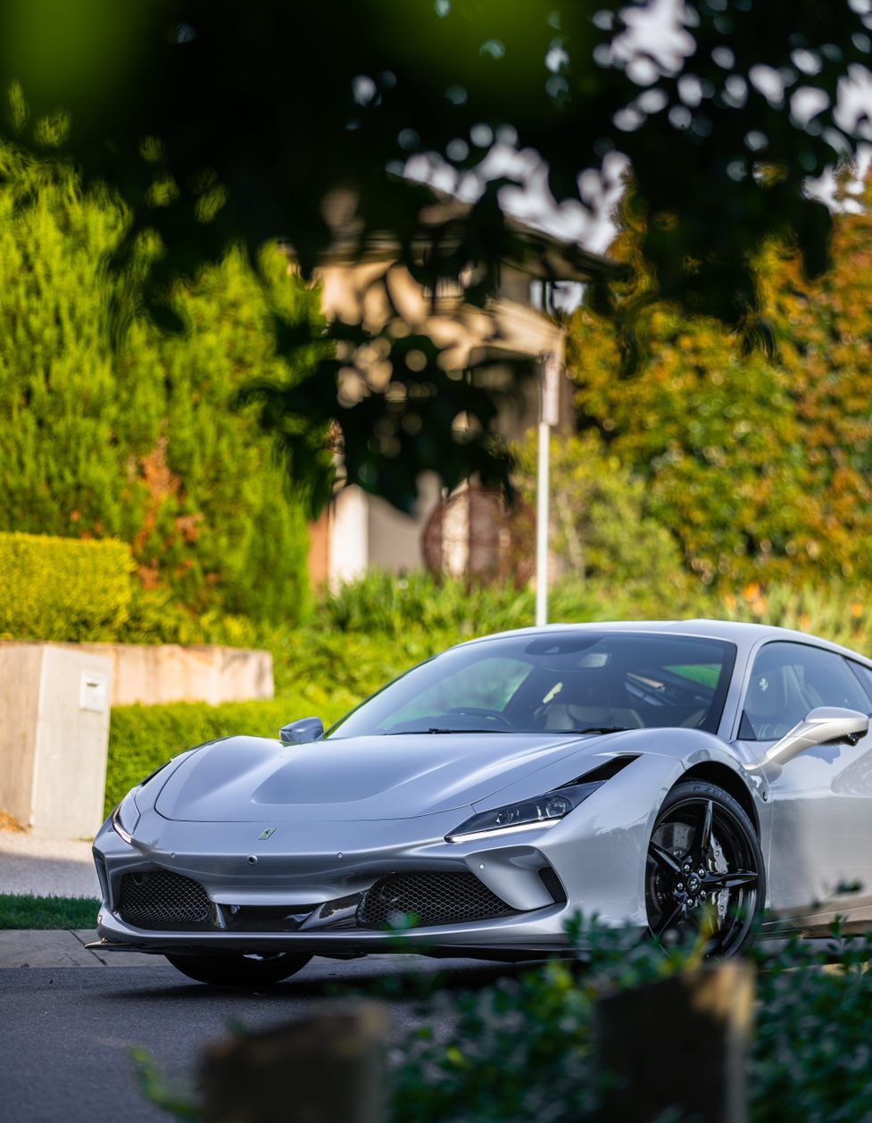 Silver Ferrari sports car parked on a road, trees and greenery in the background.