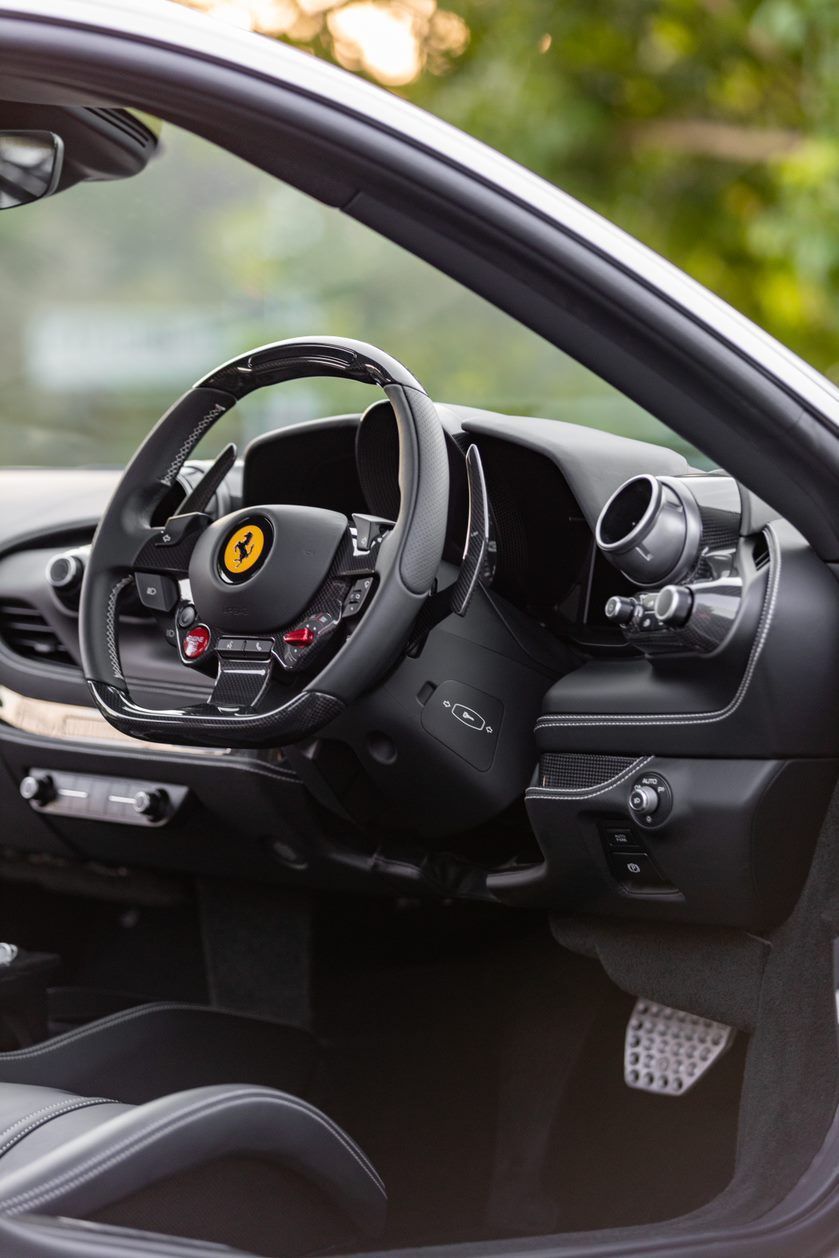 Interior of a black Ferrari sports car, showing the steering wheel with the Ferrari emblem and other controls.