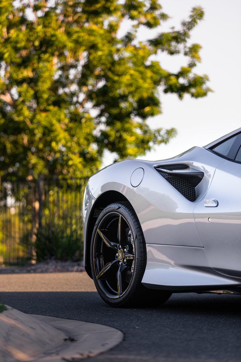 Silver sports car parked by a tree, with black wheels.