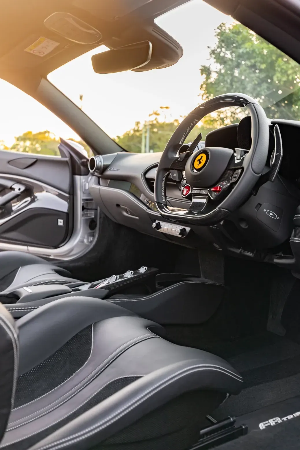 Interior of a Ferrari sports car: black leather seats, steering wheel, dashboard, and a view of the outside.