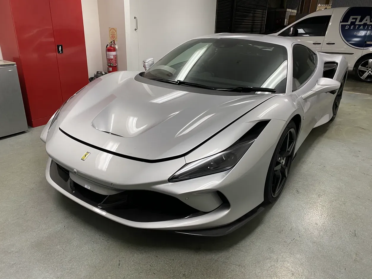 Gray Ferrari sports car parked near a garage with a person walking in the background.