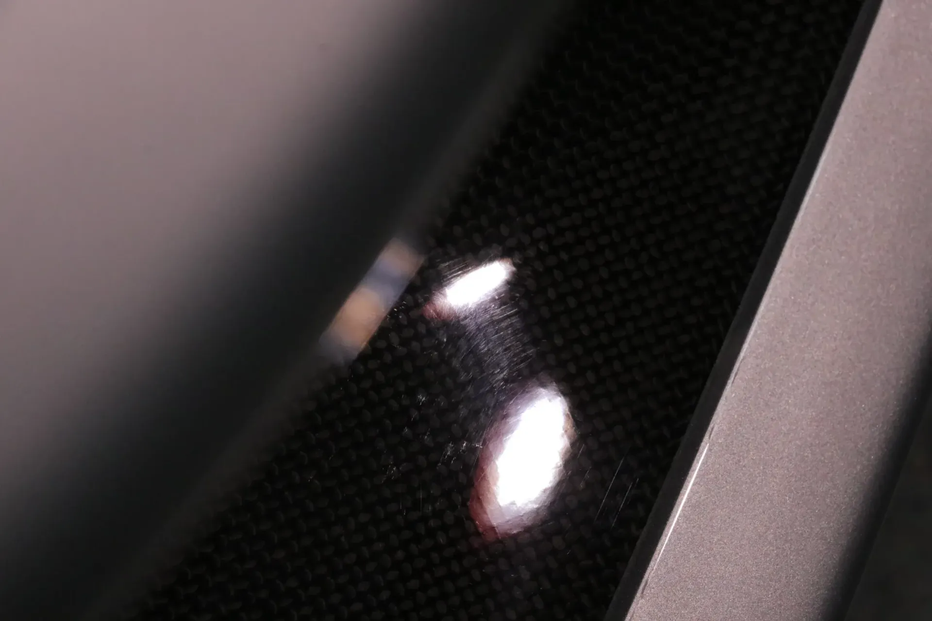 Close-up of glossy carbon fiber panel with light reflections, bordered by a gray frame.