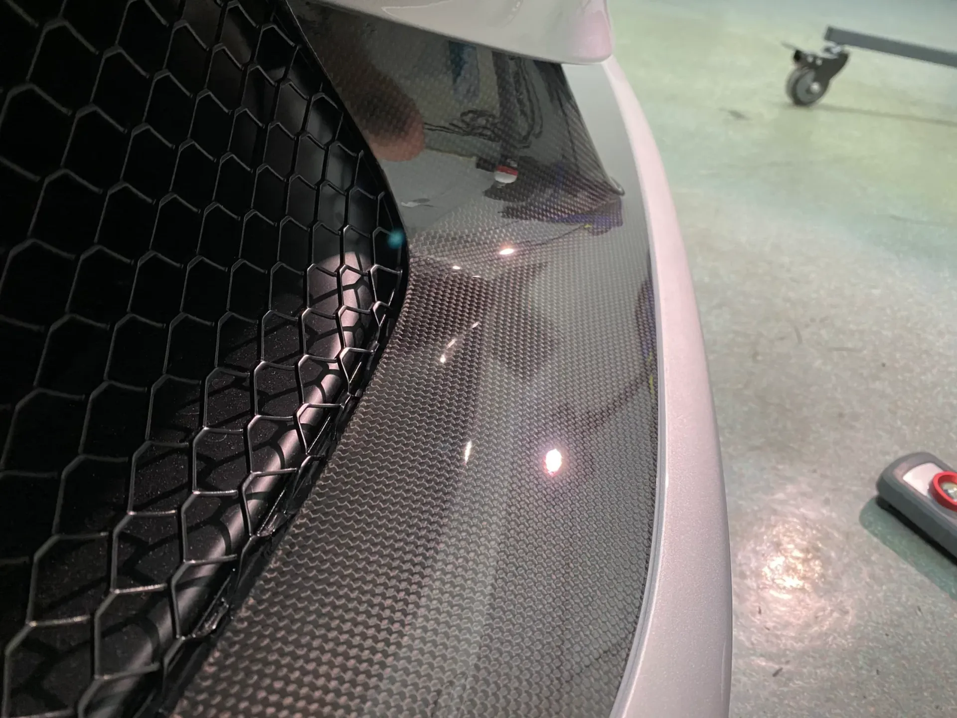 Close-up of a car bumper with carbon fiber detailing and a black mesh grille.