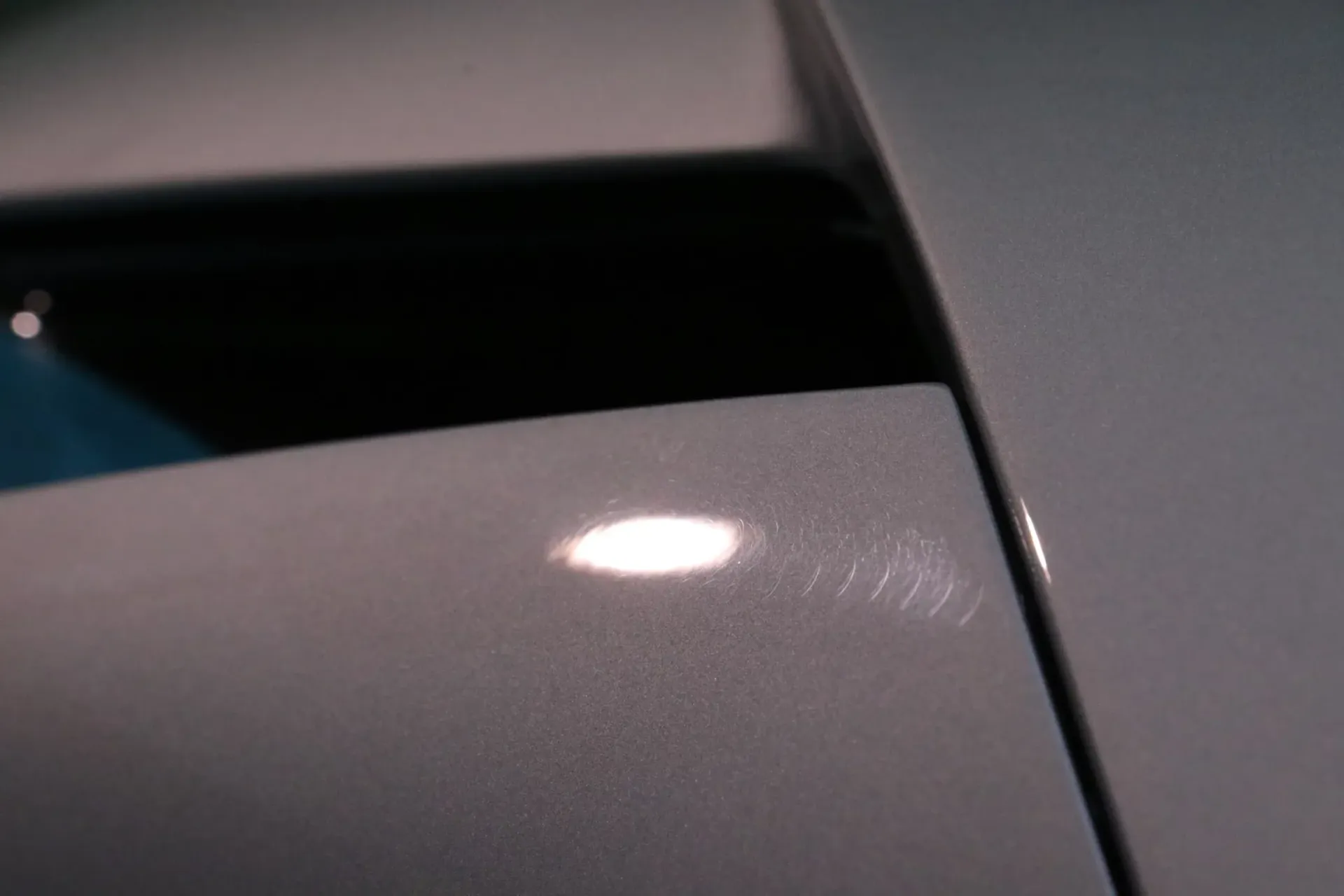 Close-up of a silver car's paint, showing scratches and a bright reflection.