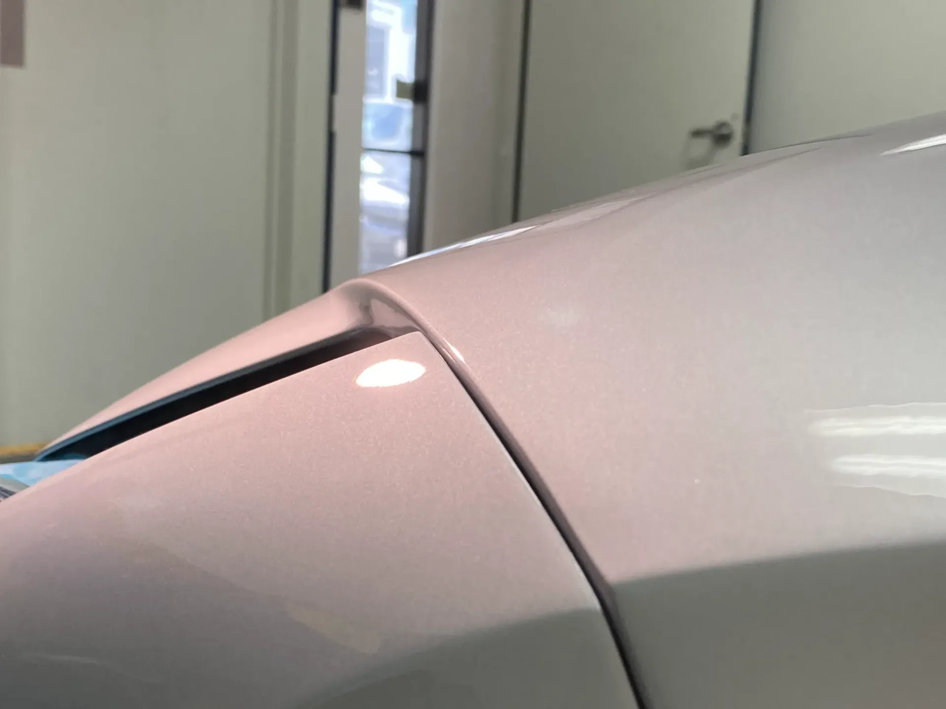White car's front panel, a detail shot showing the curve and seam where the hood meets the fender.