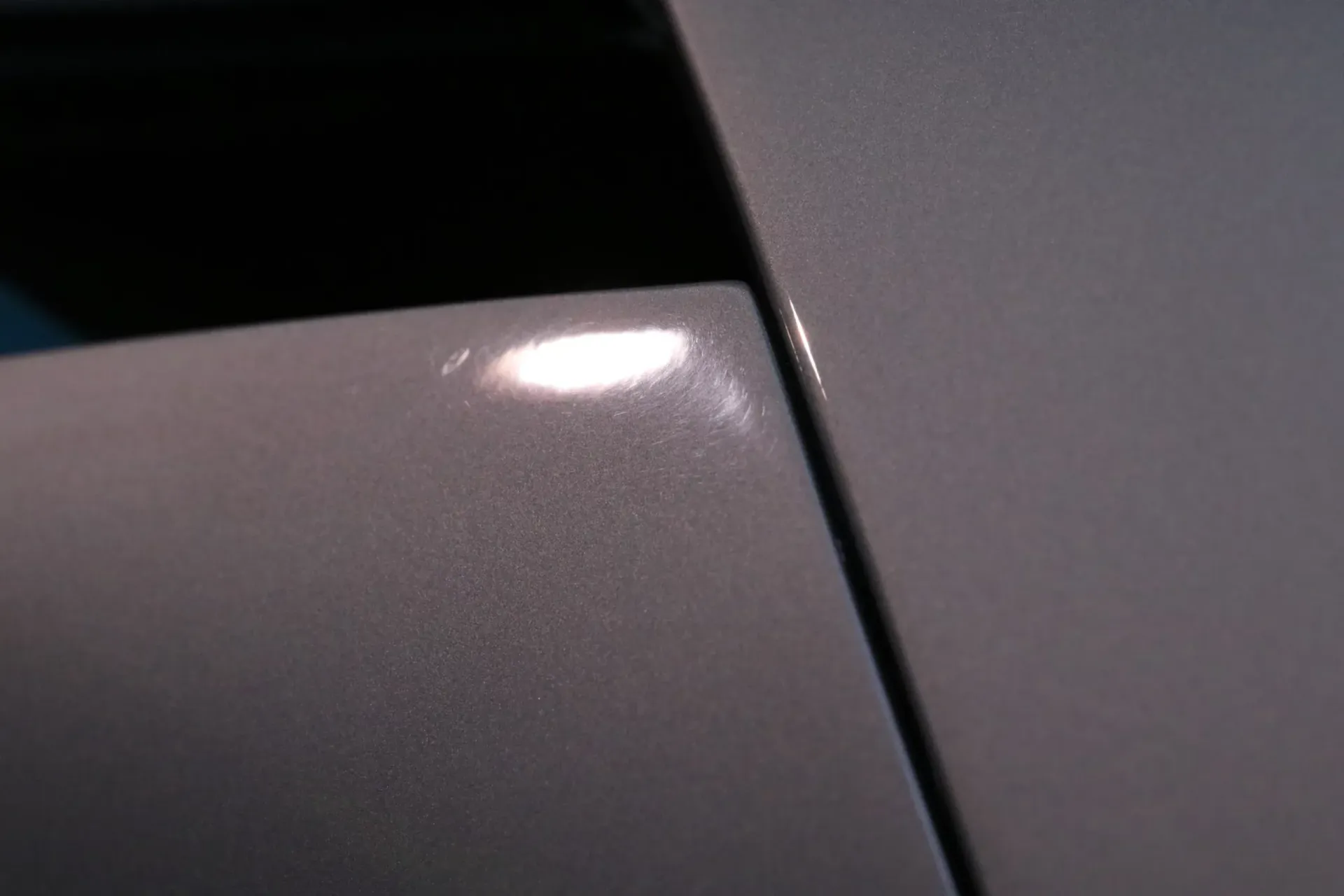 Close-up of silver car paint with a bright reflection on a curved surface.