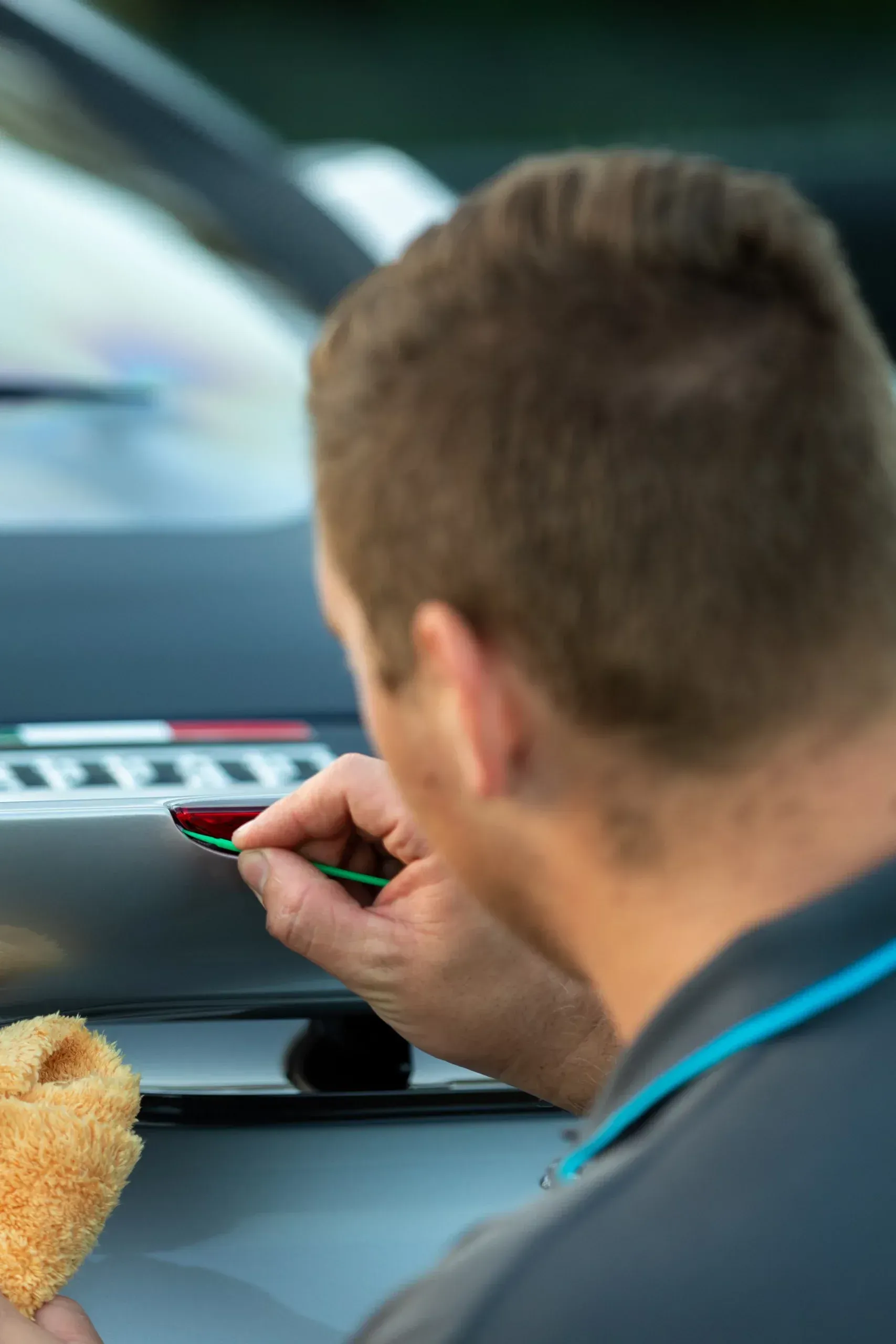 Person using a small tool to touch up a car's paint, working on the front of a vehicle.