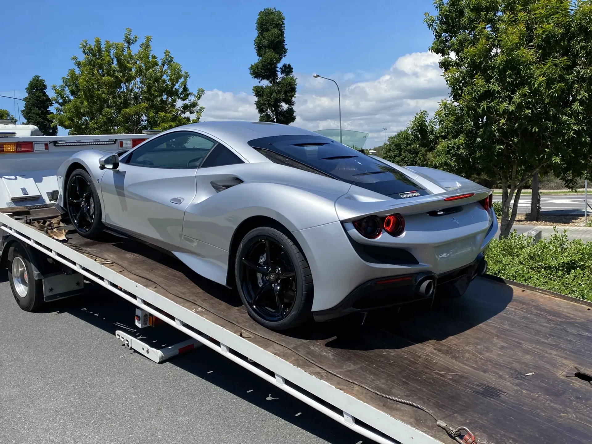 Silver Ferrari sports car on a tow truck, outdoors.