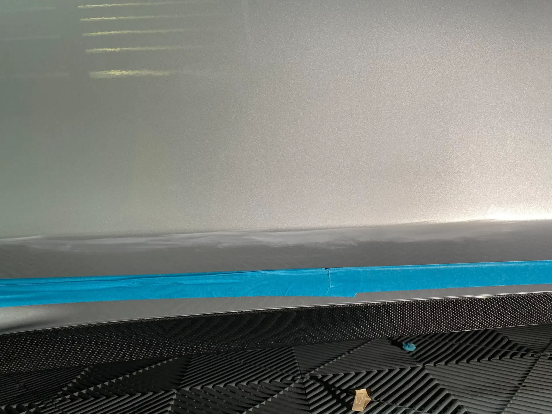 Silver car surface, blue tape, and black textured material.